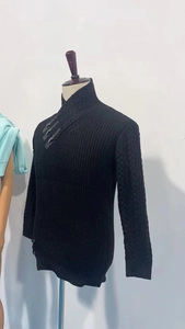 Detail of men's chunky black knit sweater featuring cable patterns and leather buckles