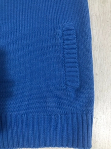 Detail view of royal blue knit sweater showing side pocket and ribbed hem on wood background