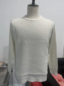 Detailed macro shot of white waffle knit sweater fabric with ribbed round neck and cuffs