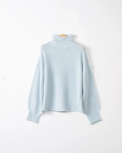 Dettaglio di un maglione a maglia grossa azzurro con collo alto e spalle calate