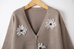 Dettaglio di un cardigan in maglia marrone con ricami floreali bianchi e perline