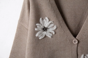 Dettaglio ravvicinato del cardigan cammello con toppa floreale e perline applicate