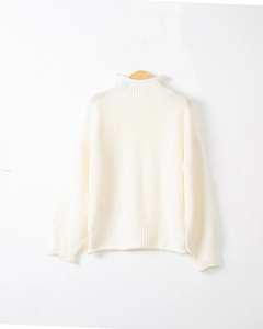 Dettaglio del maglione bianco a collo alto con trama a maglia grossa su gruccia in legno