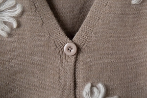 Dettaglio dello scollo a V e dei bottoni rotondi su questo cardigan ricamato color kaki