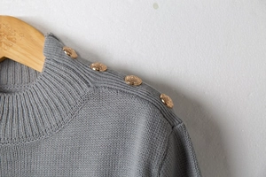 Detail of grey knit sweater showing ribbed crew neck and vintage gold metal buttons