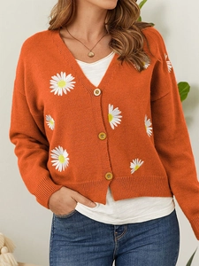 Close-up of orange-red knit cardigan featuring white daisy embroidery and yellow buttons