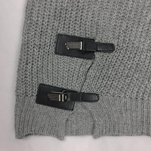 Detail of grey knit sweater showing honeycomb texture and leather buckle fasteners