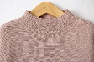 Close-up of knit turtleneck sweater in mauve showing fine fabric texture on wooden hanger