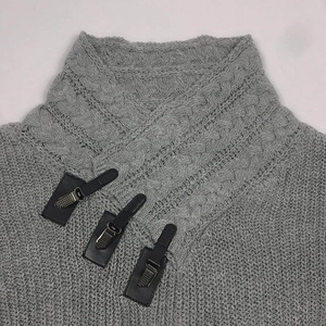 Close-up of grey knit sweater featuring decorative leather straps and metal buckles