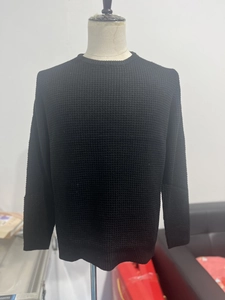 Close-up of black waffle texture knit fabric on a long sleeve round neck men's sweater