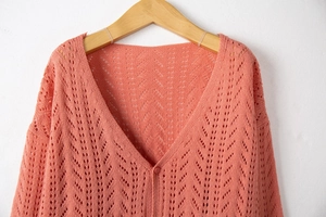 Detail of coral knit cardigan showing intricate hollow out pattern and V-neck button closure