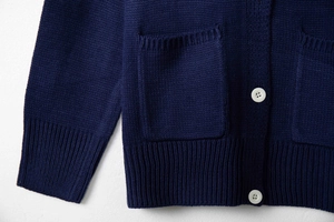 Close-up of deep blue knitted cardigan with white button and textured square pocket detail