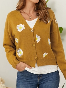 Detailed embroidery of white daisies on a mustard yellow knit cardigan with buttons