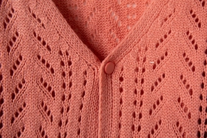 Close-up of coral knit cardigan featuring a V-neckline and intricate pointelle patterns