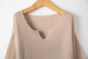 Détail du col en V festonné d'un pull en maille beige présenté sur un cintre en bois