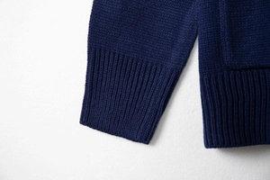 Detail of dark blue knit cardigan showing ribbed cuffs and fine stitching on white surface