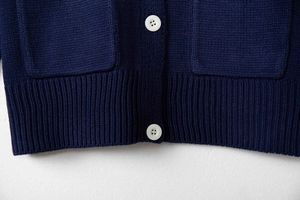 Detail of navy knit cardigan featuring white buttons and ribbed hem texture