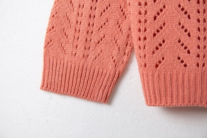 Detail of coral pink knit cardigan featuring hollow pointelle patterns and ribbed cuffs