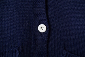 Macro shot of white four-hole button and navy blue knit texture of the women cardigan