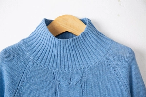 Detailed view of sky blue knit sweater showing thick cable patterns and ribbed turtleneck