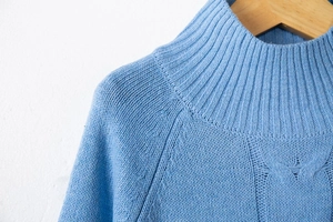 Detail of light blue cable knit sweater featuring rib-knit collar and textured patterns
