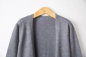 Detail of grey knitted cardigan texture on wooden hanger with textured wall background
