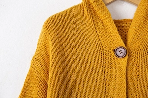 Détail d'un cardigan jaune en maille épaisse avec col côtelé et bouton de style rétro