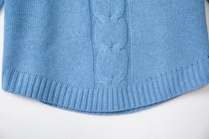 Detailed close-up of light blue cable knit sweater featuring curved ribbed hem and thick texture