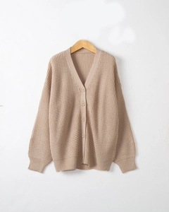 Dettaglio del tessuto cardigan in maglia beige con bottoni su gruccia di legno