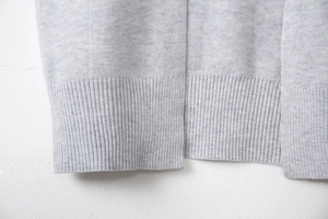 Detail shot of the light gray knit cardigan featuring a ribbed hem and flat stitching