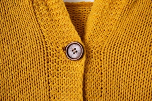 Détail du cardigan en maille jaune gingembre avec bouton en bois et texture laine