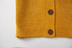 Détail macro du cardigan en maille jaune avec deux boutons en bois marron foncé
