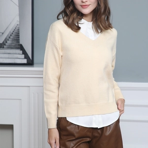 Elegant women's V-neck cream knit sweater styled with layered white shirt and leather pants