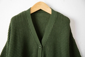 Dettaglio macro del cardigan in maglia a nido d'ape verde scuro con bottoni coordinati