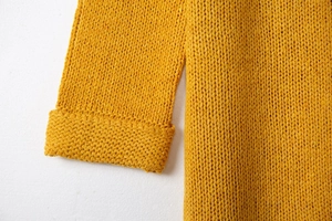 Détail du tricot épais et des poignets roulés d'un gilet long de couleur jaune moutarde