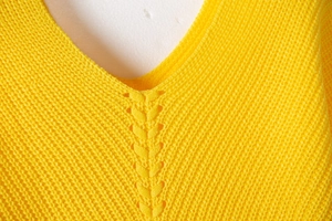 Detail of V-neck knitted sweater with openwork weaving in vibrant yellow fabric