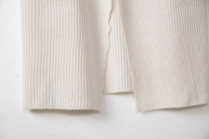Detailed close-up of cream white knit cardigan hem featuring ribbed texture and side slit