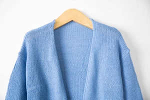 Close-up of sky blue chunky knit cardigan texture with classic weave on a wooden hanger