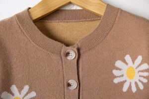 Close-up of brown knit cardigan featuring white daisy floral patterns and marble buttons