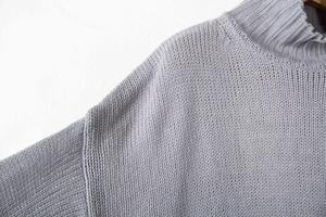 Dettaglio di un maglione grigio lavorato a maglia con collo alto e spalle scese morbide