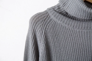 Detail of grey turtleneck sweater featuring thick rib knit texture and raglan sleeve seams