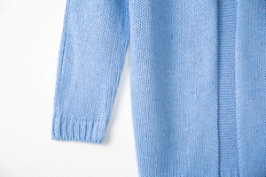 Close-up detail of sky blue chunky knit cardigan with ribbed cuffs and textured stitch