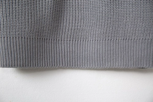 Close-up detail of grey knitted sweater showing rib-knit hem and tight stitching texture
