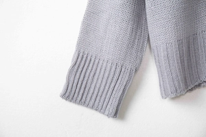 Dettaglio di un maglione in maglia grigio chiaro con polsini a costine e trama spessa