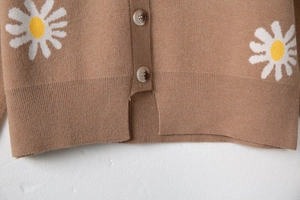 Detail of brown knit cardigan featuring white daisy floral patterns and marble buttons