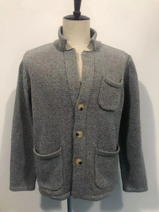 Detail der grauen Grobstrickjacke mit drei bernsteinfarbenen Knöpfen und Taschen