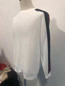 Détail de maille gaufrée blanche avec rayures bleu et rouge sur les manches du pull