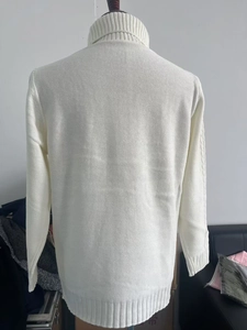 Close-up of white turtleneck sweater featuring cable knit patterns and ribbed cuffs