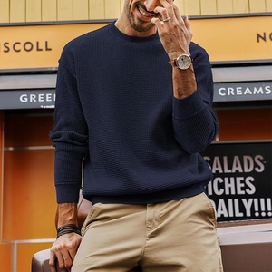 Detailed waffle texture of dark blue crewneck sweater with ribbed cuffs on outdoors model