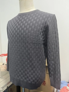 Detail of dark grey men's knit sweater featuring textured checkerboard pattern and ribbed cuffs